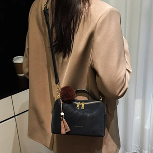 Détail latéral du sac bandoulière en cuir noir avec pompon en peluche et breloque gland