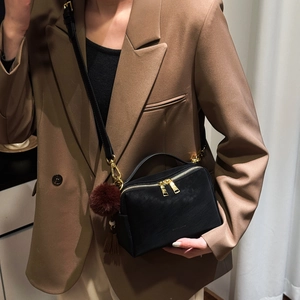 Détail du sac bandoulière noir avec fermetures dorées et pompon décoratif en peluche