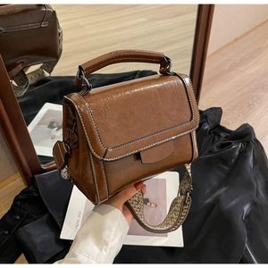 Detail der dunkelbraunen Lederhandtasche mit weißen Kontrastnähten und Web-Schultergurt
