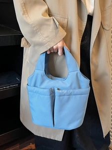 Light blue nylon tote bag with front pockets shown in a casual lifestyle setting
