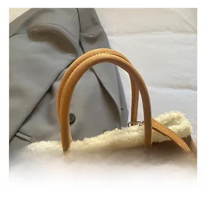 Close-up of brown suede handbag featuring plush white faux fur trim and leather top handle