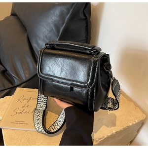 Details der schwarzen glänzenden Handtasche mit Kontrastnaht und geometrischem Gurt