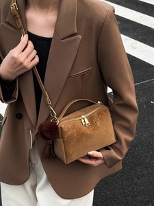 Sac bandoulière rétro en daim caramel avec pompons et détails dorés porté par un mannequin