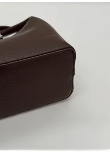 Detail of the widened flat base and pebbled leather texture of this brown bucket bag