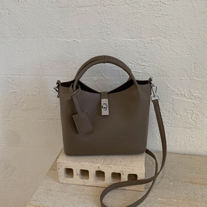 Detailed macro view of litchi textured taupe leather bucket bag with silver twist lock
