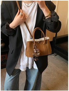 Detail view of brown leather bucket bag with white fleece trim and leopard charm
