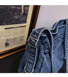 Close-up of blue denim shoulder bag with AITING embroidery and adjustable metal buckles
