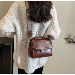 Nahaufnahme der braunen Vintage-Leder-Vierecktasche mit gewebtem Gurt auf einem weißen Pullover