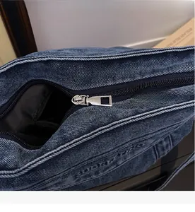 Close-up of smooth metal zipper and embossed branding on deep blue denim shoulder bag