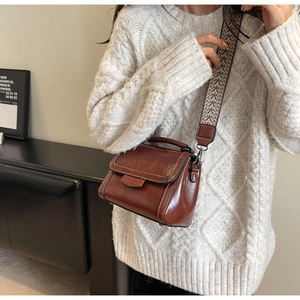 Details einer braunen Vintage-Lederhandtasche mit geometrisch gemustertem breitem Tragegurt