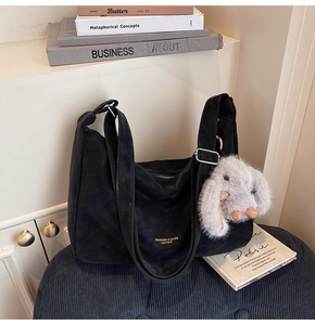 Detalle de bolso tote de ante negro con letras doradas y un colgante de conejo peludo