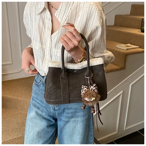Close-up of brown suede bucket bag with white faux fur trim and monster plush charm