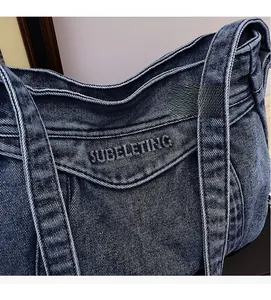 Detail of dark blue washed denim fabric with letter embroidery on the shoulder bag