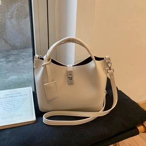 Detail of cream lychee leather bucket bag with silver twist lock on soft grey cushion