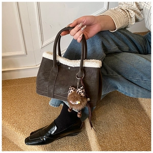 Detail of dark brown tote bag with white plush trim and leopard print charm accessory