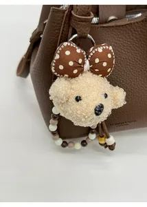 Detail of plush bear charm with polka dot bow and beaded strap on a bucket bag