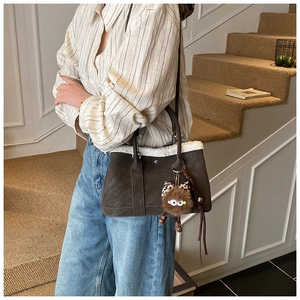 Detail view of dark coffee suede bucket bag with white faux fur trim and plush charm