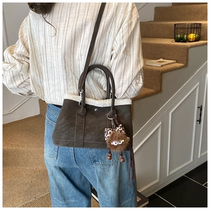 Detail of a brown suede crossbody bag with white faux shearling trim and plush pendant