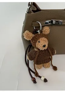 Close-up of a brown teddy bear plush charm with knit sweater on a leather bag