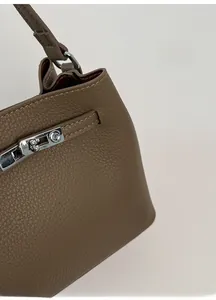 Close-up of litchi grain leather texture and silver twist-lock buckle on brown bucket bag