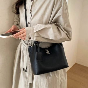 Detailed view of a black pebbled leather bucket bag with metal clasp worn by a model