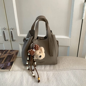 Detail of taupe bucket bag featuring lychee grain leather and a cute plush bear charm