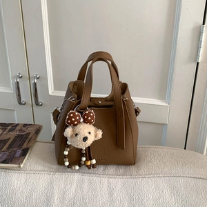 Close-up of brown pebbled leather bucket bag with cute plush bear charm in living room