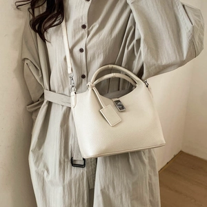 Detail of a creamy white leather bucket bag with silver lock on a model outfit