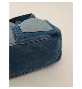 Detailed macro view of reinforced denim bag bottom with blue patchwork and brown stitching