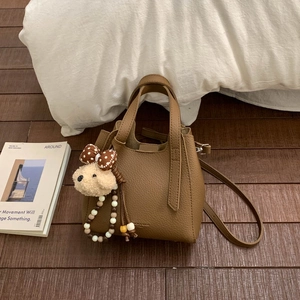 Brown lychee leather bucket bag with a plush bear charm on a cozy indoor setup