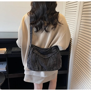 Model view of black washed denim crossbody bag featuring embroidered text and saddle shape