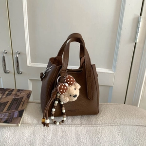 Close-up of brown litchi pattern leather bucket bag with cute plush bear charm