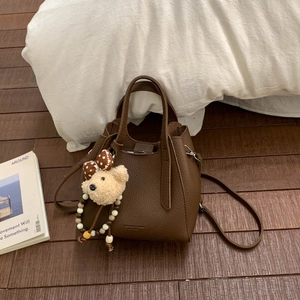 Detail of brown litchi leather bucket bag with cute teddy bear charm on wood floor