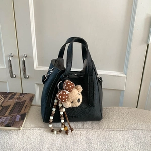 Detail of black pebble leather bucket bag with plush bear charm and beaded chain