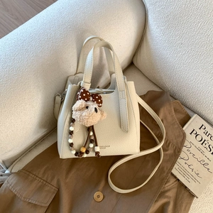 Detail of cream bucket bag featuring lychee texture and cute plush bear charm accessory