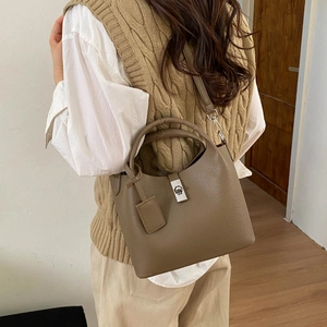 Detail of taupe pebbled leather bucket bag featuring silver turn-lock and crossbody strap