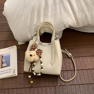 Detail of cream white leather bucket bag with cute bear charm and detachable strap