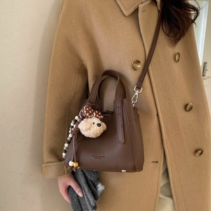Brown litchi grain bucket bag detail with plush bear charm and fashion text print
