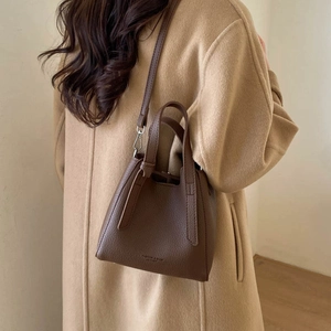 Detailed view of a dark brown litchi pattern bucket bag styled with a camel winter coat