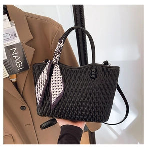 Detalle de bolso acolchado negro con un pañuelo de seda decorativo en el asa superior