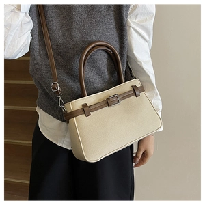 Détail d'un sac à main structuré beige avec poignées brunes et boucle en métal sur la bandoulière