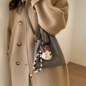 Detail of grey litchi leather bucket bag featuring a cute teddy bear charm and bead strap