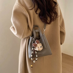 Gray pebble leather bucket bag with cute bear charm shown on camel wool coat back view