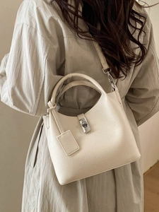 Cream leather bucket bag with metallic twist lock and adjustable shoulder strap worn by model