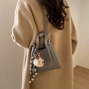 Detail of grey pebble leather bucket bag with plush bear charm worn with camel coat