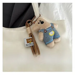 Close-up of a cute plush bear charm with denim overalls on a white leather tote bag