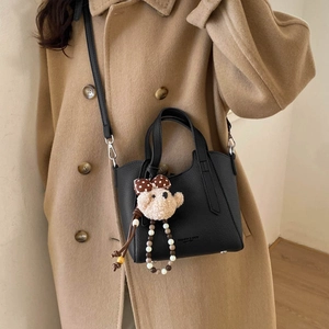 Detail of black pebbled leather bucket bag featuring a plush bear and pearl charm