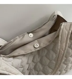 Detail of beige quilted tote bag showing magnetic silver buckle and herringbone lining