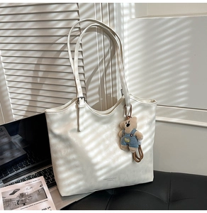 Detail of cream white leather tote bag with a cute brown bear charm and metal buckle