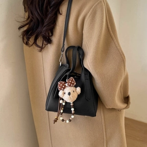 Detail of black pebbled leather bucket bag with cute bear charm worn on camel coat